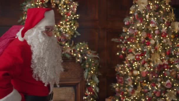 Zeitlupe eines Mannes im Weihnachtsmannkostüm, der eine Tasche im Zimmer hält und in die Kamera blickt — Stockvideo