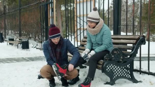 Zorgvuldig vriendje helpt jonge vrouw met schaatsen tijdens outdoor date in winterpark — Stockvideo