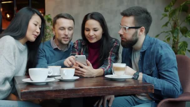 Neşeli gençler sohbet ediyor ve gülüyor. Kafede akıllı telefon kullanarak eğleniyorlar. — Stok video