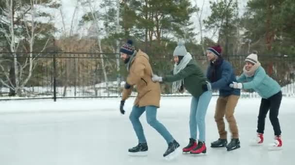 Ευτυχισμένοι νέοι με χειμωνιάτικα ρούχα παγοδρομία στο παγοδρόμιο του πάρκου γελώντας απολαμβάνοντας υγιή δραστηριότητα — Αρχείο Βίντεο