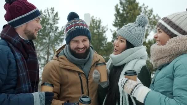 Cheerful girls and guys enjoying winter day outdoors clinking coffee cups laughing in park — Stock Video