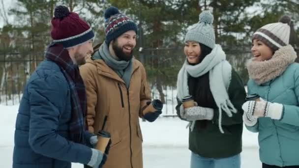 Счастливые молодые люди разговаривают держа кофе, а затем делать "дай пять" в зимнем парке — стоковое видео