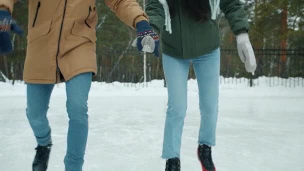 Inclinación de feliz pareja caucásico hombre y asiático mujer patinaje sobre hielo riendo al aire libre en parque — Vídeo de stock