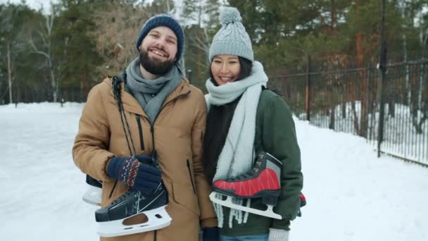 Portrait au ralenti d'une femme asiatique et d'un homme caucasien tenant des patins à glace dans un parc enneigé — Video