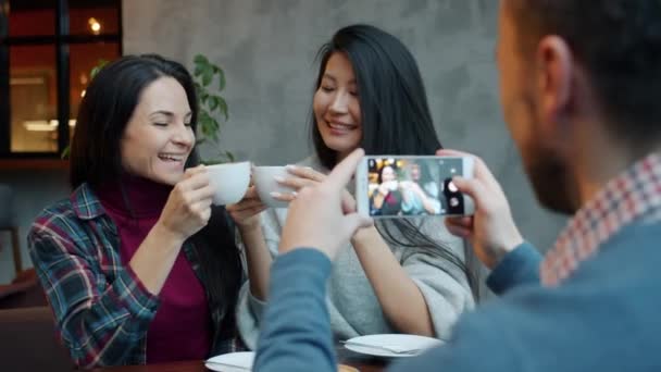 Adam, kafeteryada kahve fincanlarıyla poz veren kadın arkadaşlarının fotoğraflarını çekiyor. — Stok video