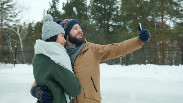 Feliz joven pareja multiétnica tomando selfie en pista de patinaje posando para la cámara del teléfono inteligente — Vídeo de stock