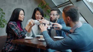 Mutlu gençler kahve fincanlarını tokuşturup gülerken, arkadaşları kafede akıllı telefonla fotoğraf çekiyor.