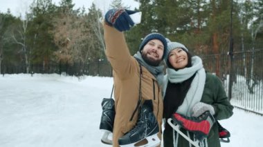 Akıllı telefon kamerası için poz veren kadın ve erkeğin dışarıda buz pateni tutarak selfie çekmesi.