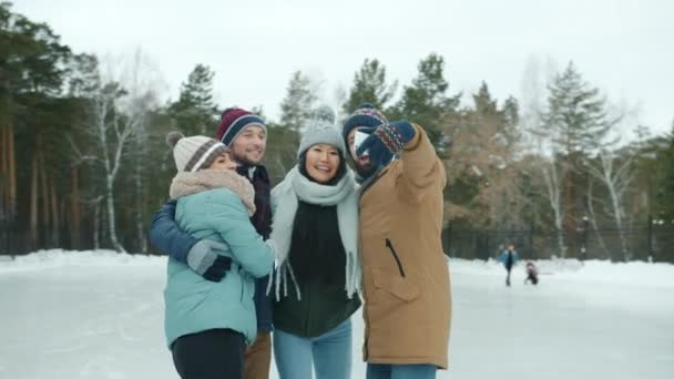 Joven tomando selfie con amigos en pista de patinaje sobre hielo usando cámara de teléfono inteligente — Vídeo de stock