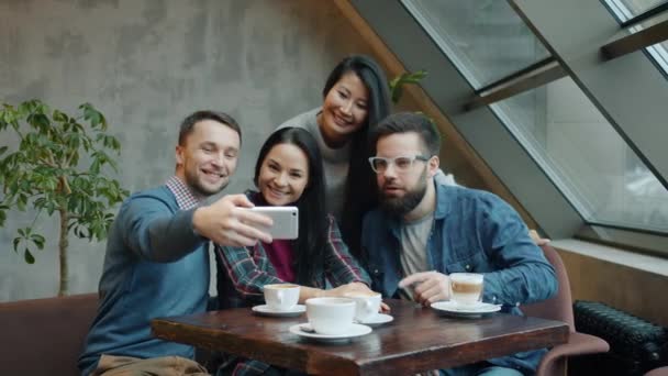 面白い顔とジェスチャーを持つスマートフォンカメラのポーズでカフェで自撮りしている友人のグループ — ストック動画