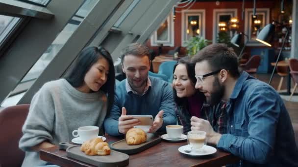 Groupe multi-ethnique de jeunes qui regardent l'écran du smartphone parler et rire dans un café — Video