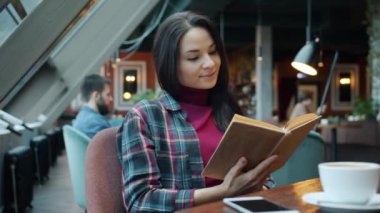 Kitap okuyan zeki genç bir kadın kafede oturmuş edebiyattan zevk alıyor.