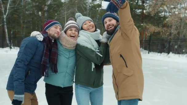 Movimiento lento de amigos felices grupo multiétnico tomando selfie en pista de patinaje sobre hielo en invierno — Vídeo de stock