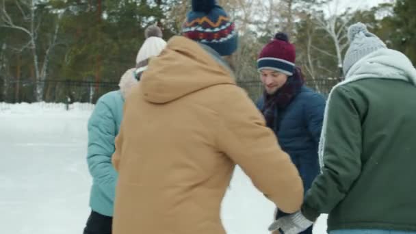 Смеющиеся девушки и парни в теплой одежде катаются на коньках в парке, наслаждаясь свежим воздухом — стоковое видео