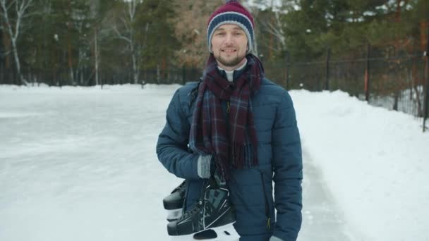 Retrato em câmera lenta de cara bonito com patins de gelo de pé ao ar livre no parque sorrindo — Vídeo de Stock