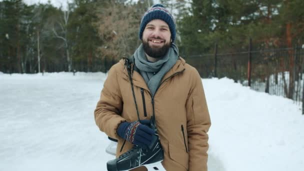 Retrato de cara atraente segurando patins de gelo de pé ao ar livre no parque sozinho sorrindo — Vídeo de Stock