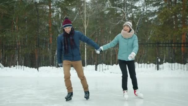 Allegro coppia uomo e donna che si tiene per mano pattinaggio su ghiaccio e parlare nel parco — Video Stock