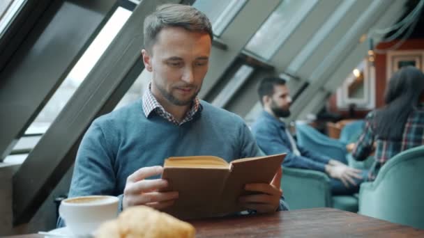 Knappe jongeman lezen boek ontspannen zitten aan tafel in cafe alleen — Stockvideo