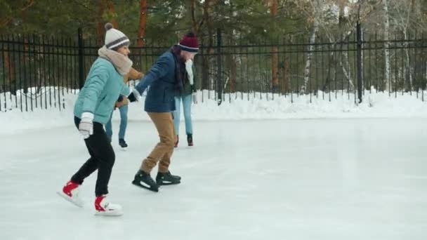 Movimiento lento de hombres y mujeres felices disfrutando del patinaje sobre hielo en el parque de invierno tomados de la mano riendo — Vídeos de Stock