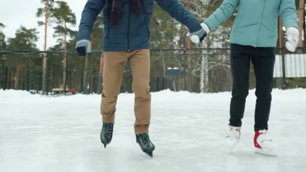 Ragazza e ragazzo in caldo inverno abbigliamento pattinaggio su ghiaccio tenendo le mani ridendo nel parco — Video Stock