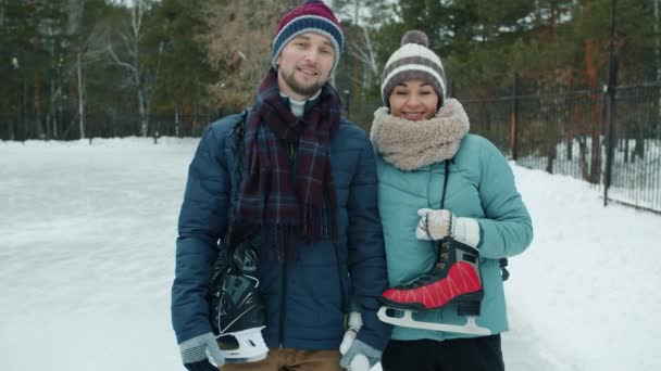 Retrato de hermosa pareja feliz chica y chico de pie al aire libre en el parque con patines de hielo — Vídeo de stock