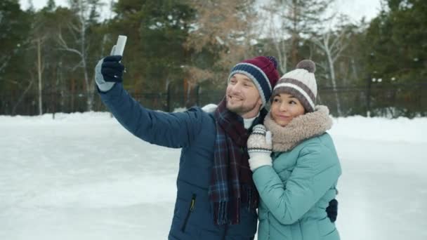 Hermosa pareja hombre y mujer tomando selfie en pista de patinaje sobre hielo con cámara de teléfono inteligente — Vídeos de Stock