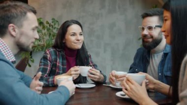Neşeli erkekler ve kadınlar sohbet ediyor ve gülüyorlar. Sıcak bir kafede kahve içiyorlar.
