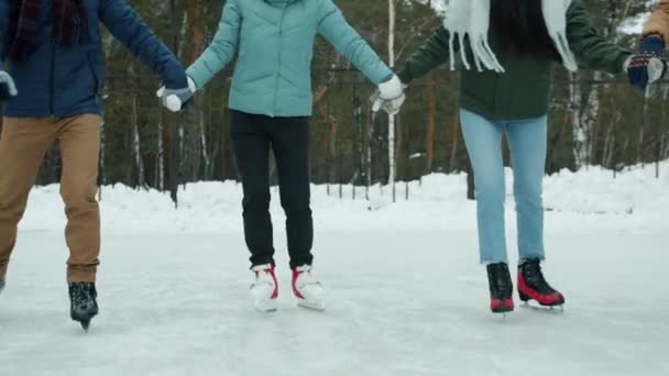 Tilt-up slow motion of happy young friends skating on frozen lake holding hands laughing — Stock Video