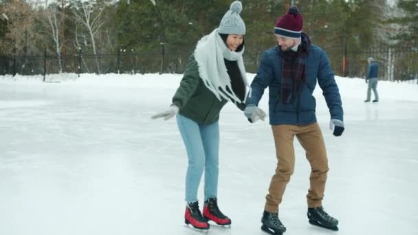 Fiatal férfi tanít barátnője jégkorcsolyázni a parkban télen fogja kezét beszél — Stock videók