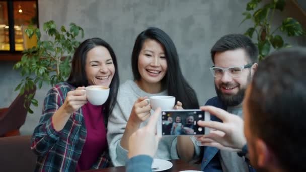 Gente alegre tazas de café tintineo celebrando en la cafetería mientras el hombre toma fotos con la cámara del teléfono inteligente — Vídeos de Stock