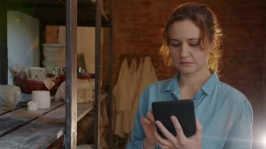 Ağır çekimde, çömlek atölyesinde tablet kullanan ciddi bir kız seramiklere bakıyor.