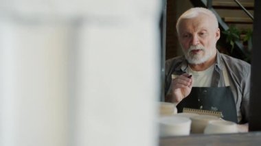 Eski bir zanaatkârın portresi atölyedeki seramikleri sayıyor ve defterde yazıyor.