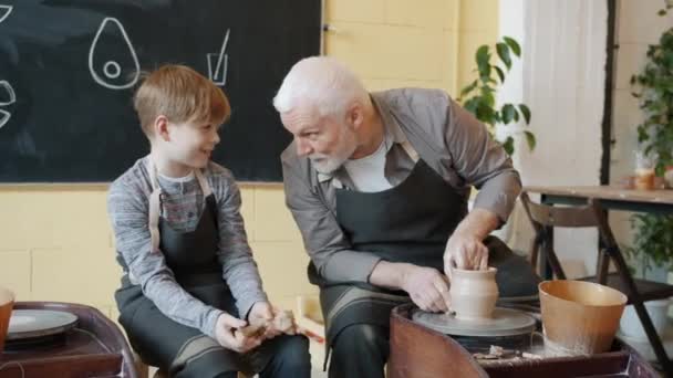 Dědeček hrnčíř dělat vázu na házecí kolo a mluvit s veselým děckem ve studiu — Stock video