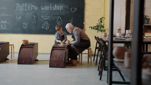 Chlapec pracující na házení kolečkem, zatímco senior muž mluví výuku v keramice workshop — Stock video