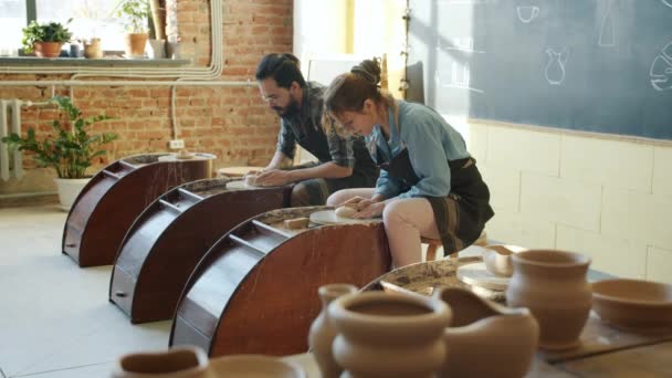 Медленное движение мужчин и женщин-керамиков, работающих с гончарными колесами в студии — стоковое видео