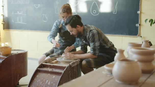 Langzame beweging van man en vrouw maken pot van spinnewiel in aardewerk workshop — Stockvideo