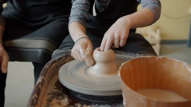 Крупный план детских рук, делающих горшок из глины под руководством взрослого гончара — стоковое видео