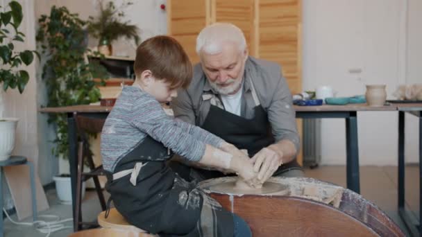 Zpomalený pohyb zkušený hrnčíř výuka malý chlapec pracovat s keramikou kolo tvarování hlíny — Stock video