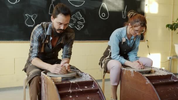 Girl and guy in aprons working with pottery wheels in studio making earthenware — Stock Video