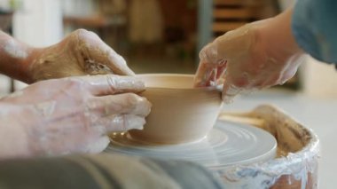 İki çift elin yakın çekimi. Erkek ve kadın, tekerin üzerindeki çamurdan kalıpları çıkarıyorlar.