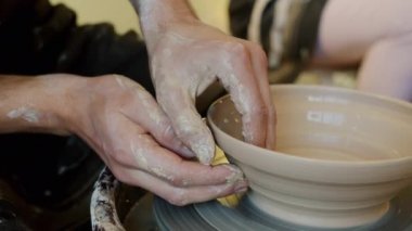 Atölyedeki çömlek çarkında killi kase yapan adamların yakın çekimi.