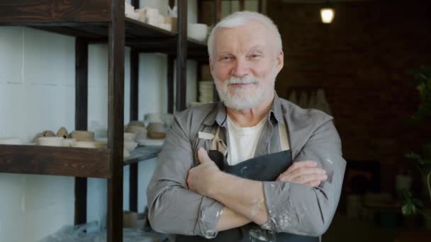Portrait of cheerful senior ceramist standing in workshop wearing apron and smiling — Stock Video