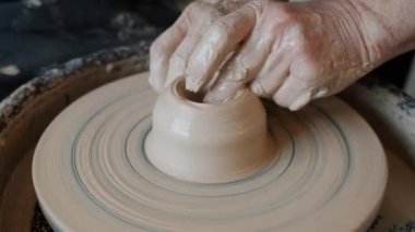 Tekerlek şekillendirme vazosunda ıslak kille çalışan yaşlı adamların yakın çekimi.
