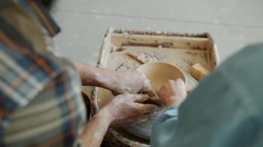 Arka planda kadın ve erkek ellerinin çömleği balçıktan şekillendirmesi ve tekerlek üzerinde birlikte çalışması.