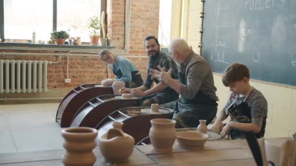 Des gens heureux parlent et travaillent avec des roues dans un atelier de poterie — Video