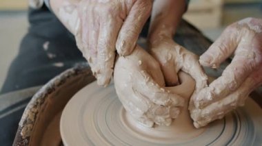 Çocuk, profesyonel çömlekçinin rehberliğinde kilden vazoya dönüşüyor.