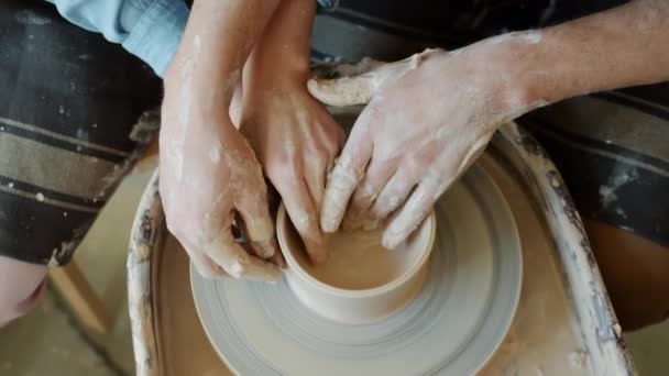 Close-up of dirty hands of man and woman molding clay making pot using throwing wheel — Stock Video