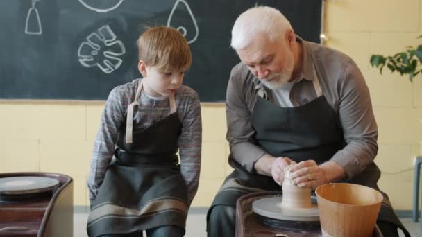 Langzame beweging van grootvader het maken van keramische vaas in aardewerk studio terwijl kleinzoon kijken — Stockvideo