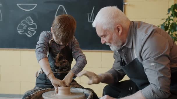 Dziadek i wnuk produkujący ceramiczny garnek z gliny na kole ceramicznym — Wideo stockowe