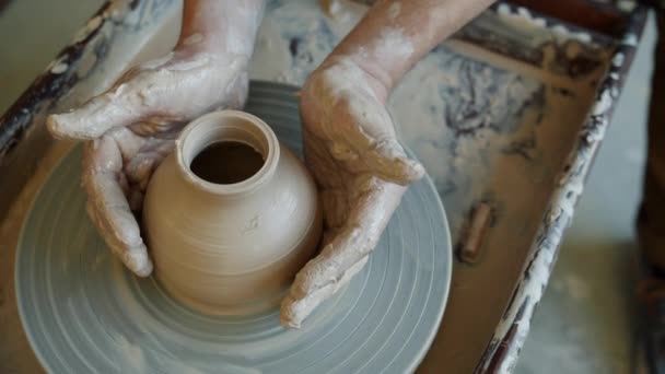 Vista ad alto angolo di mani di uomo e bella pentola in ceramica che ruota sulla ruota dei vasai — Video Stock
